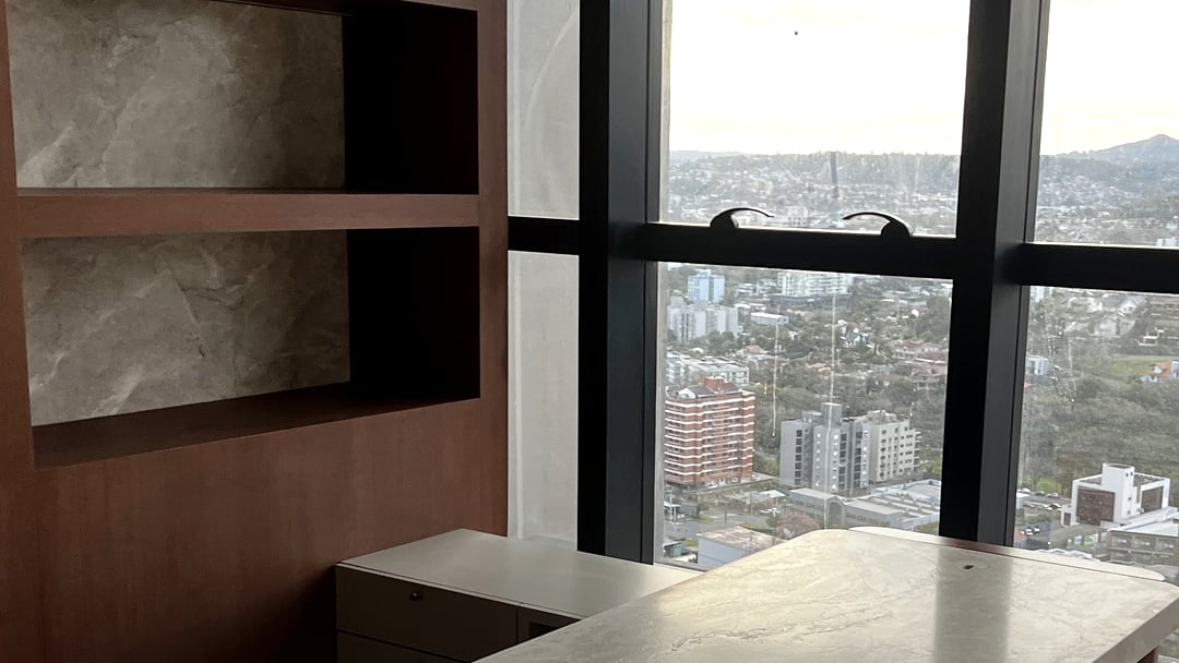 Consultório da nova clínica Neurosinos, com mesa de pedra clara, marcenaria em madeira e janela com vista para a cidade.