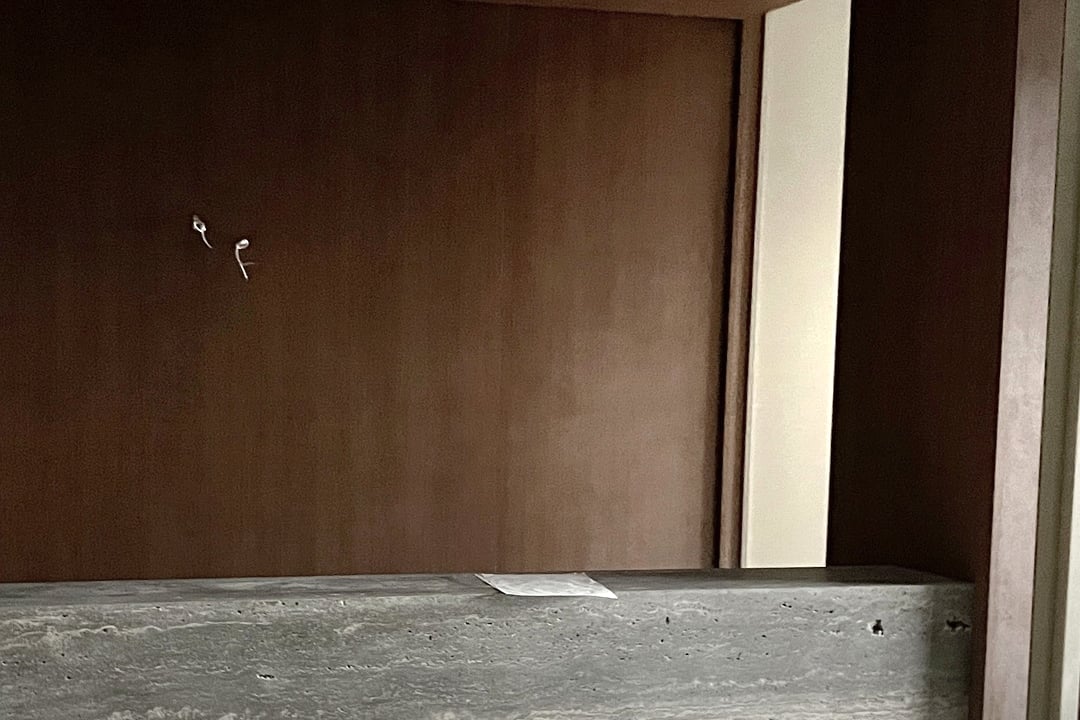 Balcão de recepção em travertino cinza, com painel de madeira ao fundo.